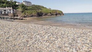 Una playa de guijarros con un edificio blanco en una colina cubierta de hierba.