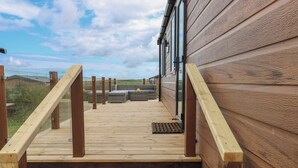 Una terraza de madera que conduce a un edificio con ventanas amplias y vistas al paisaje.