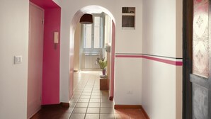A hallway with a pink wall, a white wall with a decorative stripe, and a window with a view. - Trastevere Home - Santa Maria with beautiful view on the square (Roma)