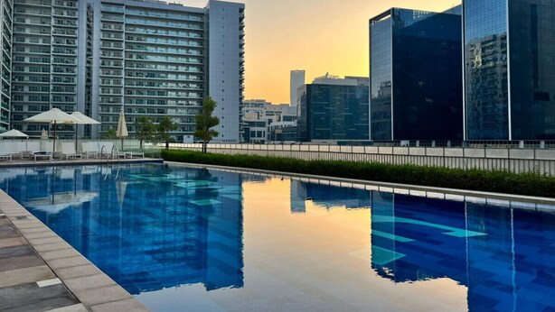 A swimming pool with a cityscape in the background, including modern buildings and a clear sky. - Soothing 1BR at Downtown Dubai Business Bay (Dubai)