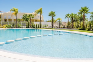 A clear blue swimming pool with circular steps leading into it, surrounded by palm trees and a fence. - Lakes 24 at Praia da Falesia Vilamoura (Loulé)