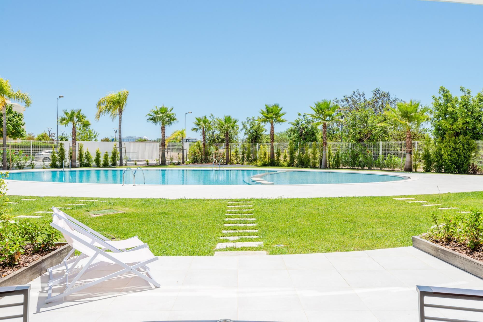 A swimming pool with a surrounding grassy area, palm trees, and a fence.