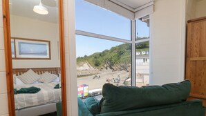 A room with a bed, a green sofa, and a large window offering a beach view.