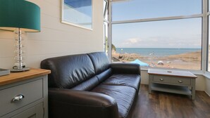 A modern living room with a leather sofa, a lamp, and a view of the beach through large windows.