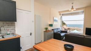A compact kitchen with a sink, a dining table, and a view of the beach through a large window.