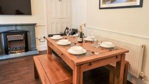 A dining room with a wooden table set for four, a fireplace, and a framed landscape painting on the wall. - 6 Calgarth View (Windermere)