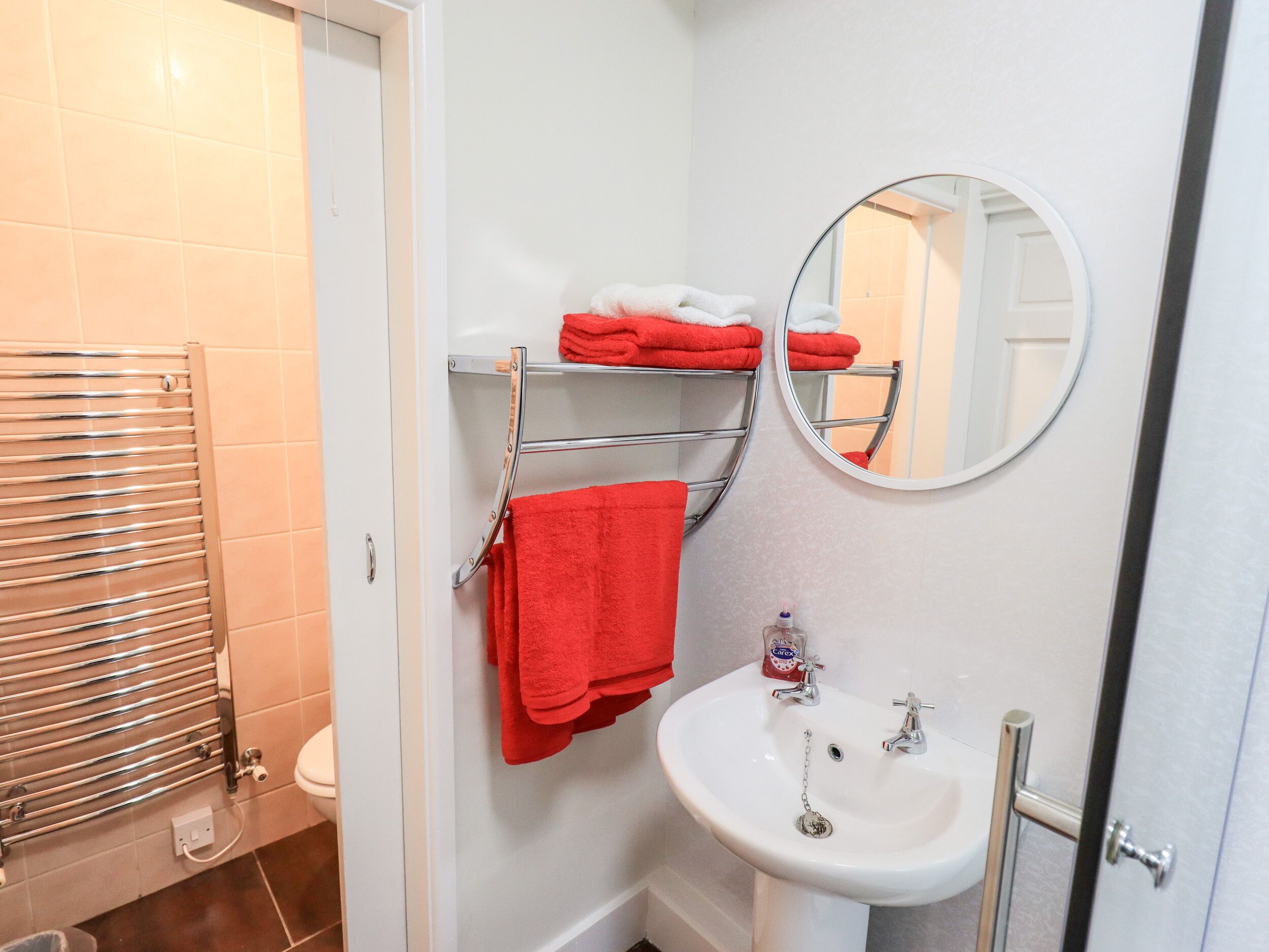 Une salle de bain avec un lavabo blanc, un miroir, un porte-serviettes avec des serviettes rouges et des toilettes.