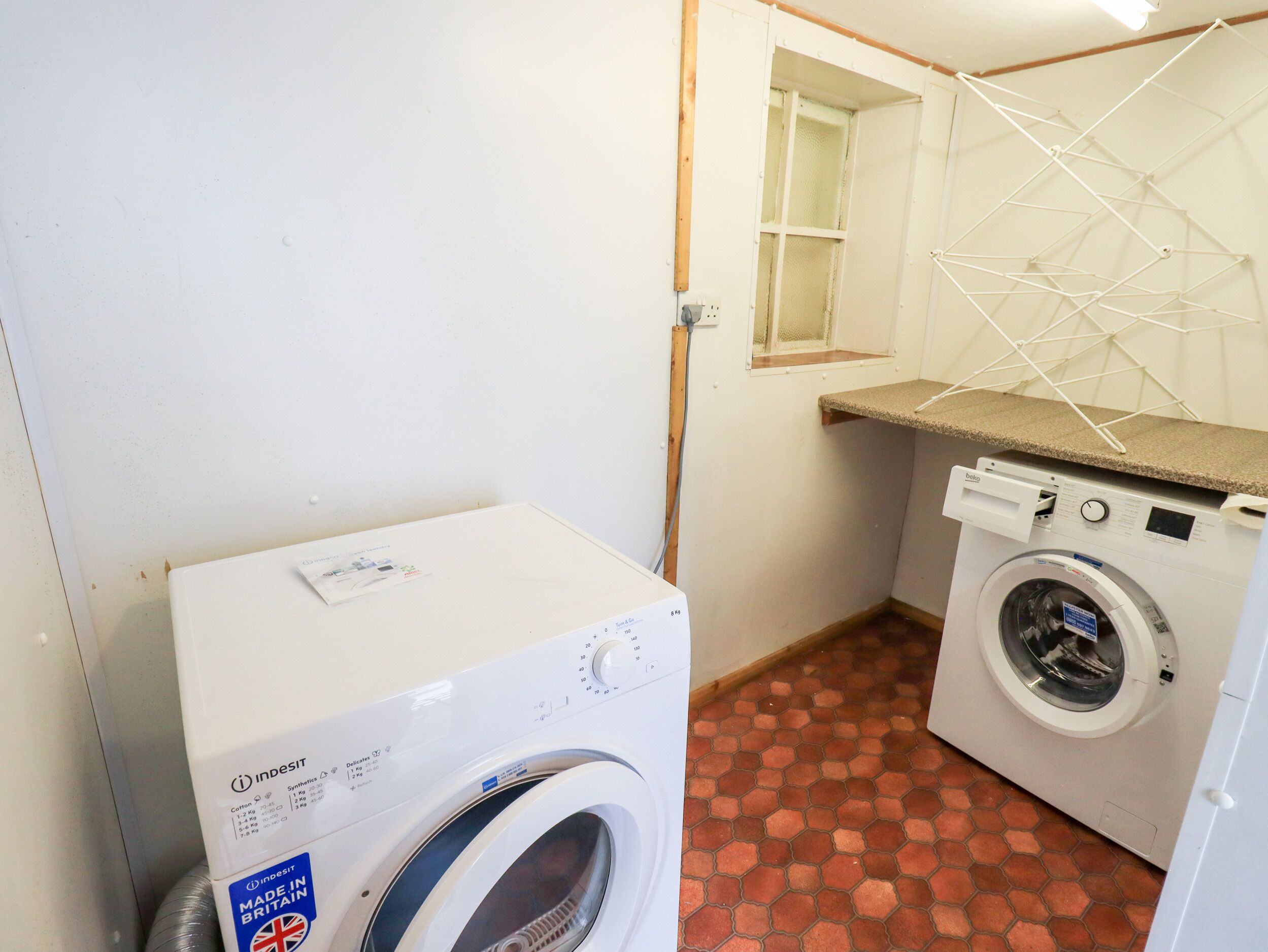 A compact laundry room with a washing machine, a dryer, and a drying rack.