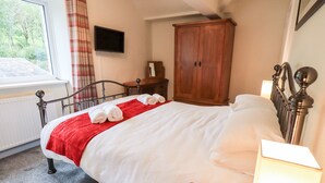 A neatly made bed with a red blanket and rolled towels, a wooden wardrobe, a bedside table with a lamp, and a window with curtains. - 6 Calgarth View (Windermere)