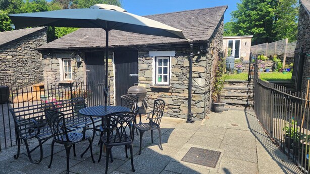 A stone building with a patio area featuring outdoor seating and a grill. - 6 Calgarth View (Windermere)
