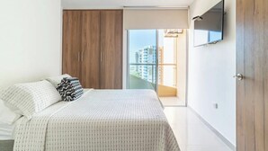 Ein Schlafzimmer mit Bett, Kleiderschrank, Fernseher und einem Balkon mit Blick auf Gebäude.