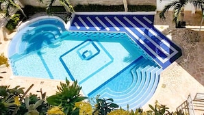 Ein geometrisch gestalteter Pool, umgeben von Pflanzen und einem gefliesten Weg.