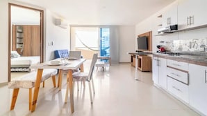Eine moderne Küche mit weißen Schränken, einem eingebauten Backofen und einer Mikrowelle. Es gibt eine Essecke mit Tisch und Stühlen sowie ein großes Fenster mit Blick auf die Stadt.