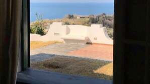 Une vue à travers la fenêtre d’un bâtiment doté d’une terrasse dallée et offrant une vue dégagée sur la mer.