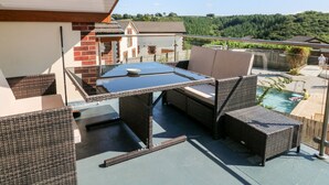 An outdoor patio with wicker furniture, a glass-top table, and a view of a swimming pool and greenery. - Hazelwood Lodge (Umberleigh)