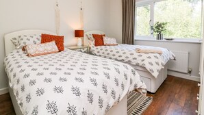 Un dormitorio con dos camas, cada una con ropa de cama estampada, una mesita de noche con lámpara, una lámpara colgante y una ventana con vistas a la vegetación.