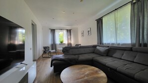 A modern living room with a large sectional sofa, a flat-screen TV, and a round wooden coffee table.