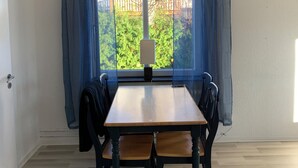 Ein Zimmer mit Holztisch und -stühlen, einem Fenster mit Vorhängen und Blick auf Grünfläche.