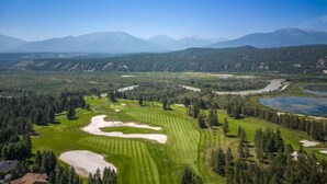 A golf course with sand bunkers, a pond, and a forested area with mountains in the background. - Alpine Retreat | Pool | Hot Tub | Affordable (Radium Hot Springs)