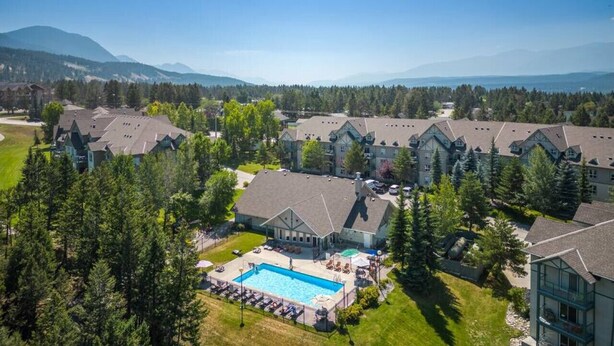 A resort with multiple buildings, a swimming pool, and a mountainous backdrop. - Alpine Retreat | Pool | Hot Tub | Affordable (Radium Hot Springs)