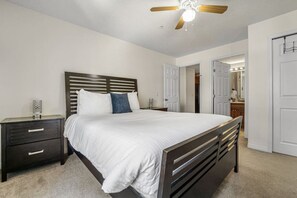 A bedroom with a bed, a nightstand, a dresser, a ceiling fan, and a door leading to another room.