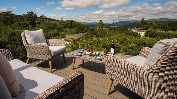 Um terraço com móveis de vime e uma mesa posta para refeição, com vista para uma paisagem exuberante.