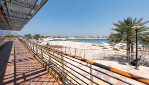 Eine Uferpromenade mit einem Kachelweg, Palmen und Strandsonnenschirmen.
