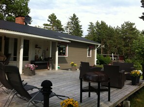 A wooden deck with outdoor furniture, a covered porch, and a brick chimney. - Cozy and Private 3-bed House With Bath Roslagen (Herräng)