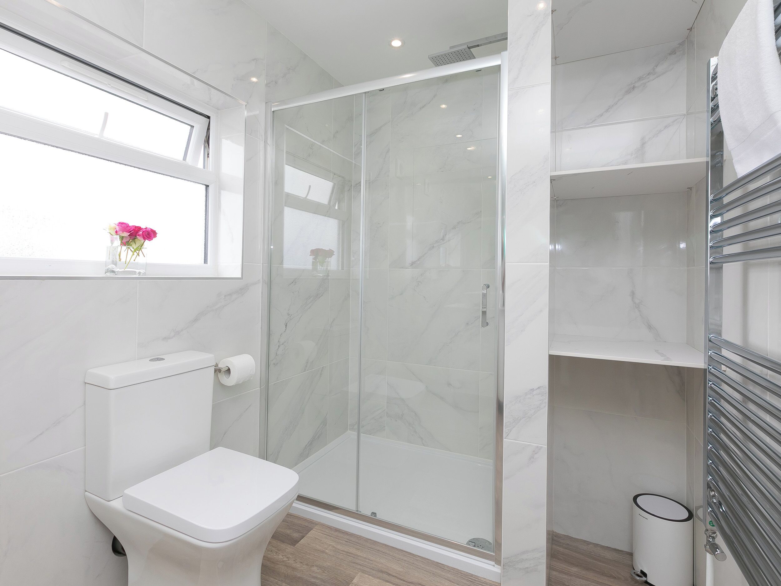 A modern bathroom with a toilet, a glass shower enclosure, and a window with a vase of flowers.