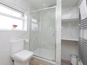 A modern bathroom with a toilet, a glass shower enclosure, and a window with a vase of flowers. - Samphire (St Ives)