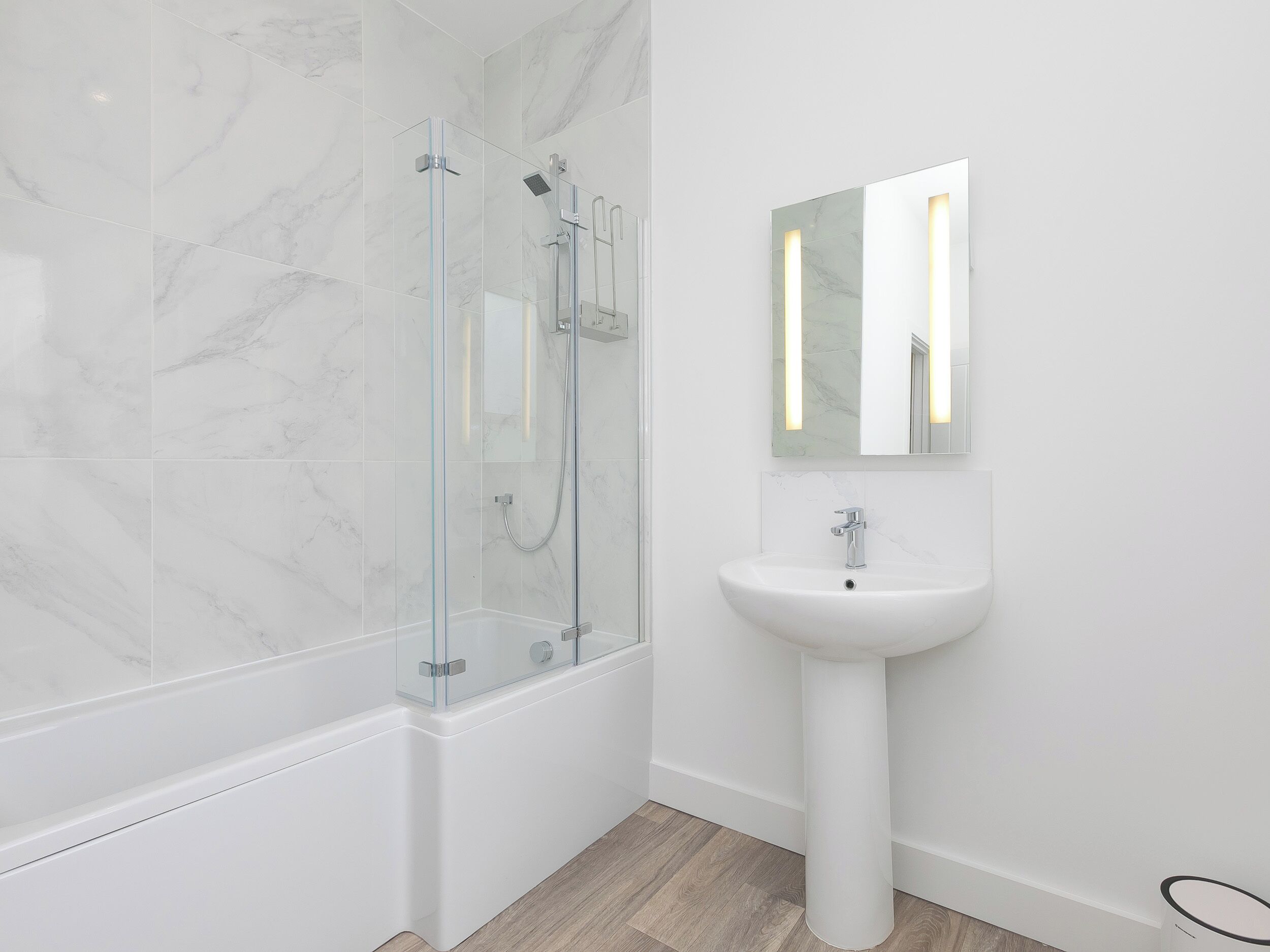 A modern bathroom with a glass-enclosed shower, a white pedestal sink, and a marble-tiled wall.