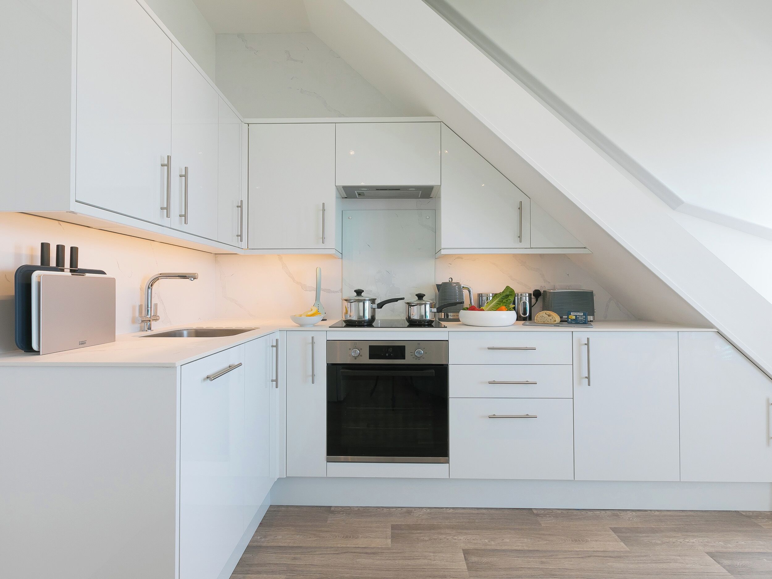 A modern kitchen with white cabinetry, a built-in oven, and a sink.