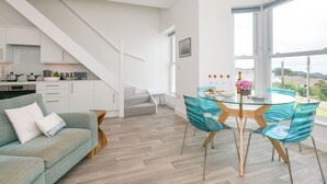 Cozinha moderna com armários brancos, uma escada e um espaço de jantar com mesa de vidro e cadeiras azul-turquesa.