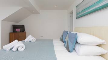 A modern hotel room with a bed, a TV, and a painting on the wall.