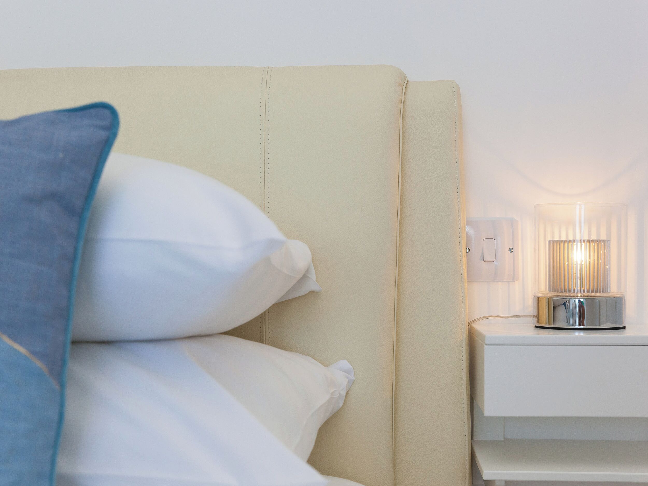 Un lit bien fait, avec des oreillers blancs et bleus, une table de chevet avec une lampe et une commode blanche.