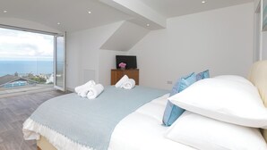 Quarto moderno com uma cama grande, uma TV em uma cômoda de madeira e uma varanda com vista para o mar.