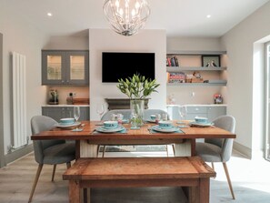A modern dining area with a wooden table set for four, a vase with green plants, and a flat-screen TV mounted on the wall. - 41 Chatsworth Gardens (Scarborough)
