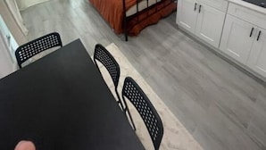 Une chambre compacte comprenant un lit, une petite table et une chaise. Elle dispose également d’une kitchenette avec des placards et un plan de travail.