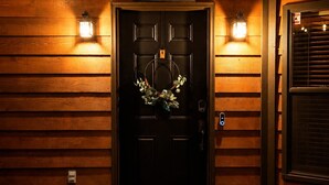 Una puerta de madera con un letrero que dice 'WELCOME' encima, una corona colgando en la puerta y un felpudo que dice 'HELLO' adelante.