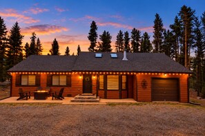A cabin with a gravel driveway, a covered patio with outdoor seating, and a garage.