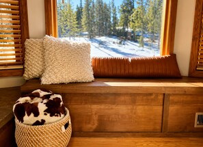 Eine Holzbank mit Blick auf einen verschneiten Wald durch ein Fenster mit Holzjalousien.