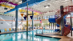 Una piscina interior con toboganes, sillas de descanso y un techo alto con vigas estructurales.