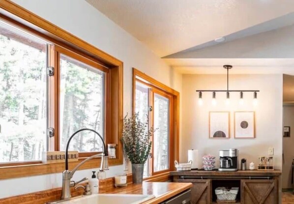 A kitchen with wooden cabinets, a sink, and a countertop. There are windows with wooden frames and a ceiling light fixture. - Cozy Family Time | BBQ | Wildlife | Hiking (Black Hawk)