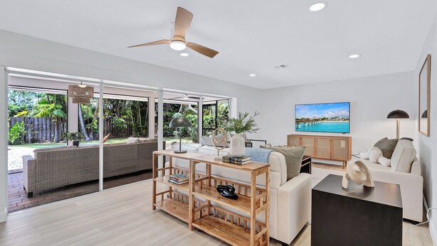 A spacious living room with a large window, a ceiling fan, a flat-screen TV, and a modern sofa.