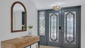 A hallway with a wooden console table, a mirror, and a door with decorative glass panels.