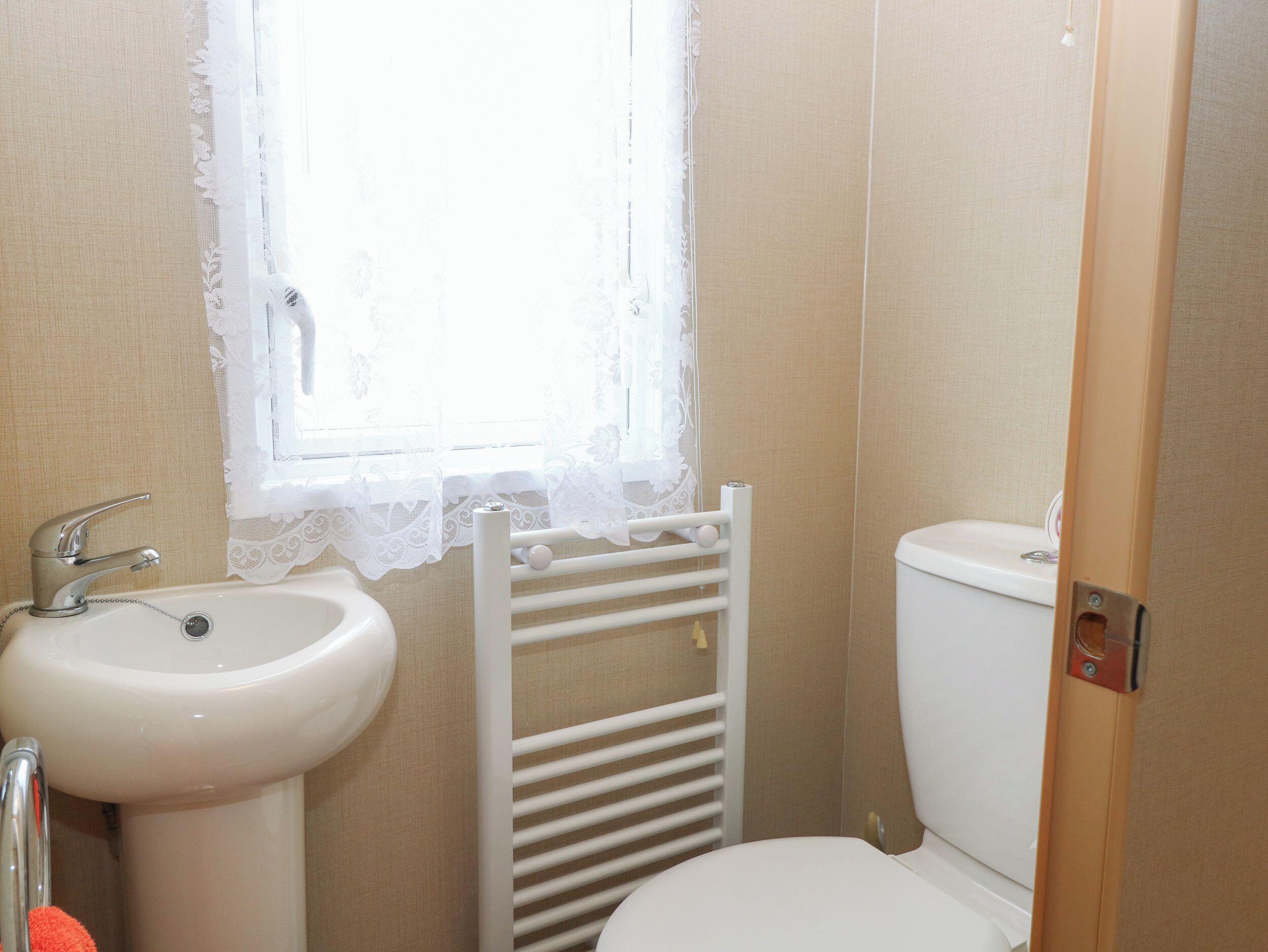 Ein Badezimmer mit Waschbecken, Toilette und einem Fenster mit Spitzenvorhängen.