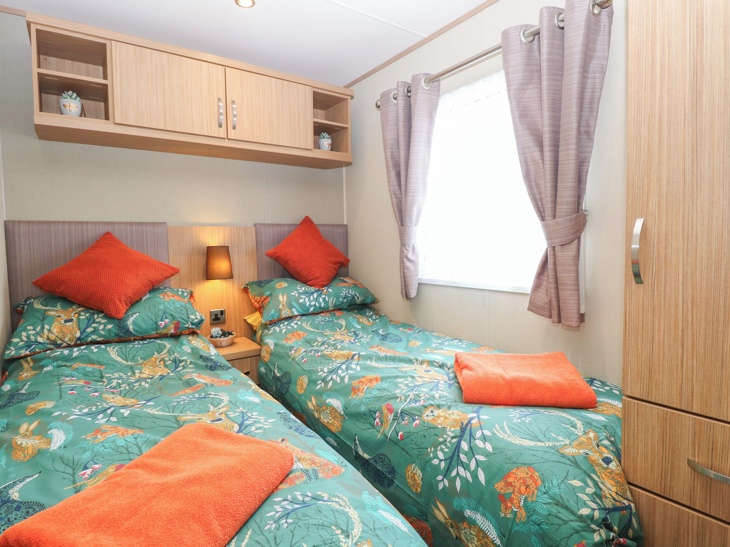 A bedroom with two beds, a wardrobe, a shelf with plants, and a window with curtains.