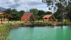 A lakeside cabin with a red roof, surrounded by greenery and a clear sky.