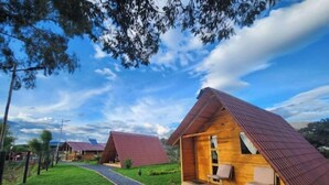 A row of wooden cabins with pitched roofs, a gravel path leading to them, and a clear blue sky.