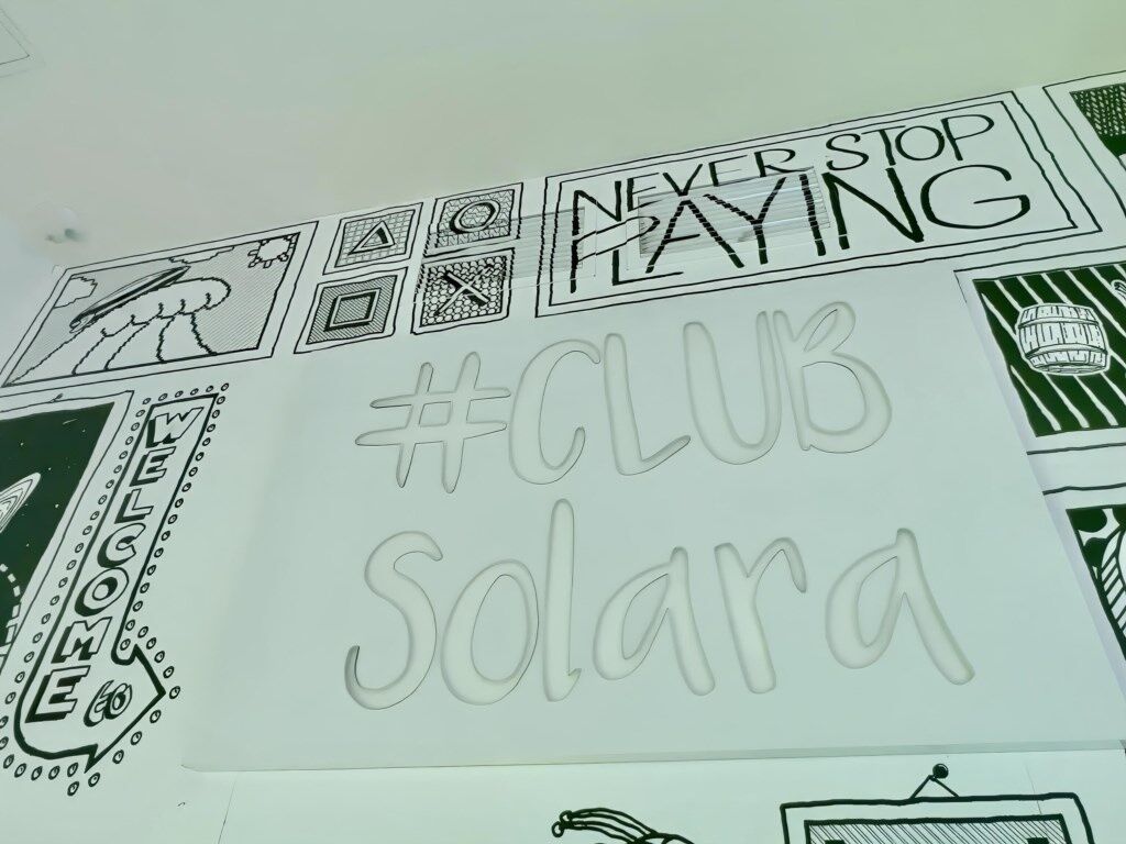 A wall with various black and white drawings and text, including 'NEVER STOP PLAYING' and '#CLUB SOLARA'.